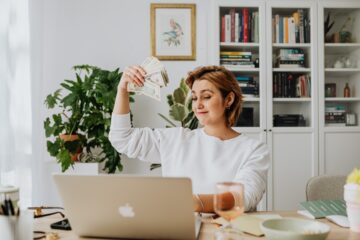 vrouw zit met een stapel geld achter een computer, als afbeelding bij een blog over lijfrente of sparen