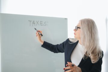 vrouw schrijft het woord taxes op een whiteboard als afbeeld bij een blog over box 1 2 en 3